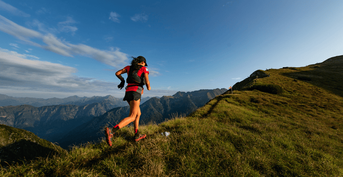 A woman running up a steep mountain, with a trail winding behind her